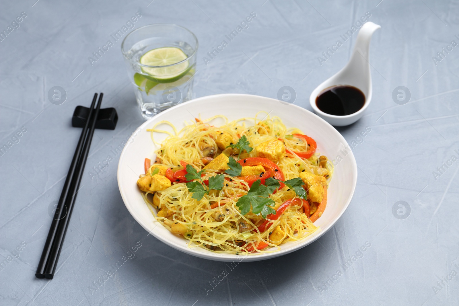 Photo of Stir-fry. Delicious cooked noodles with chicken and vegetables in bowl served on gray textured table