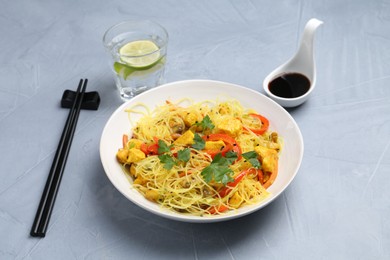 Photo of Stir-fry. Delicious cooked noodles with chicken and vegetables in bowl served on gray textured table