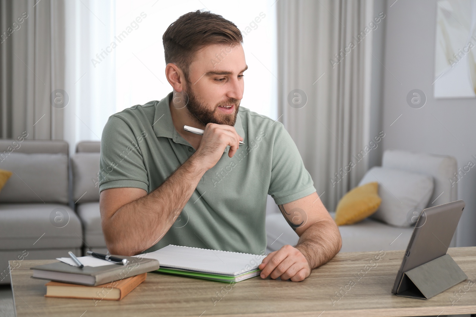 Photo of Young man watching online webinar at table indoors