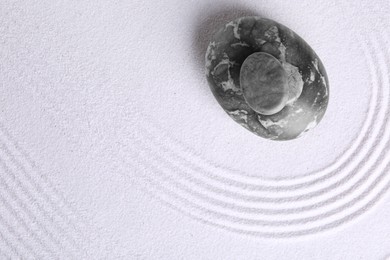 Photo of Zen garden stones on white sand with pattern, top view. Space for text