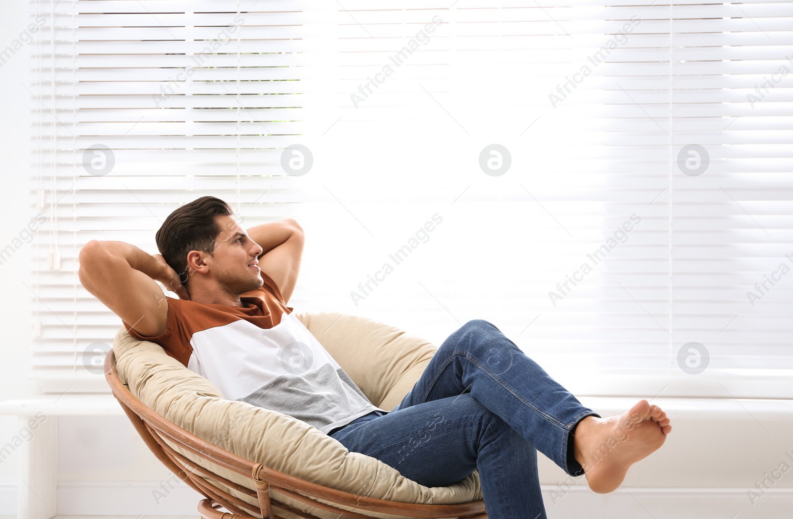 Photo of Attractive man relaxing in papasan chair near window at home