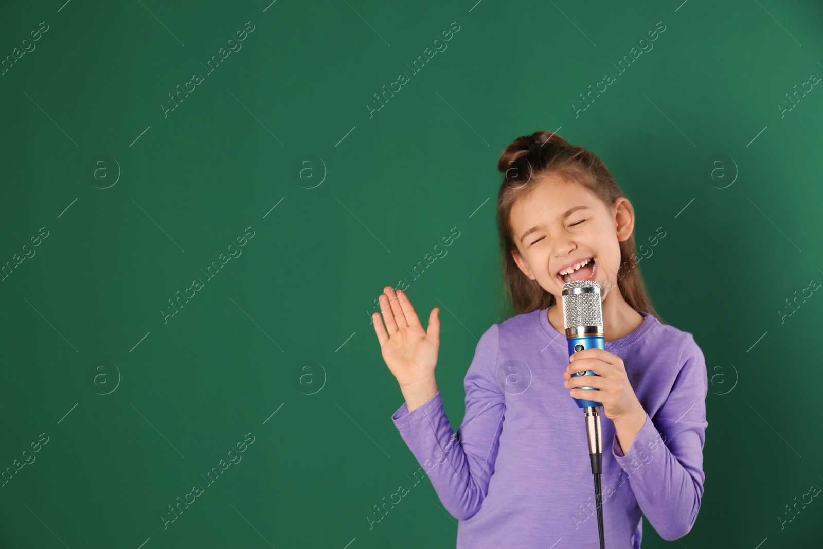 Photo of Cute funny girl with microphone on color background. Space for text