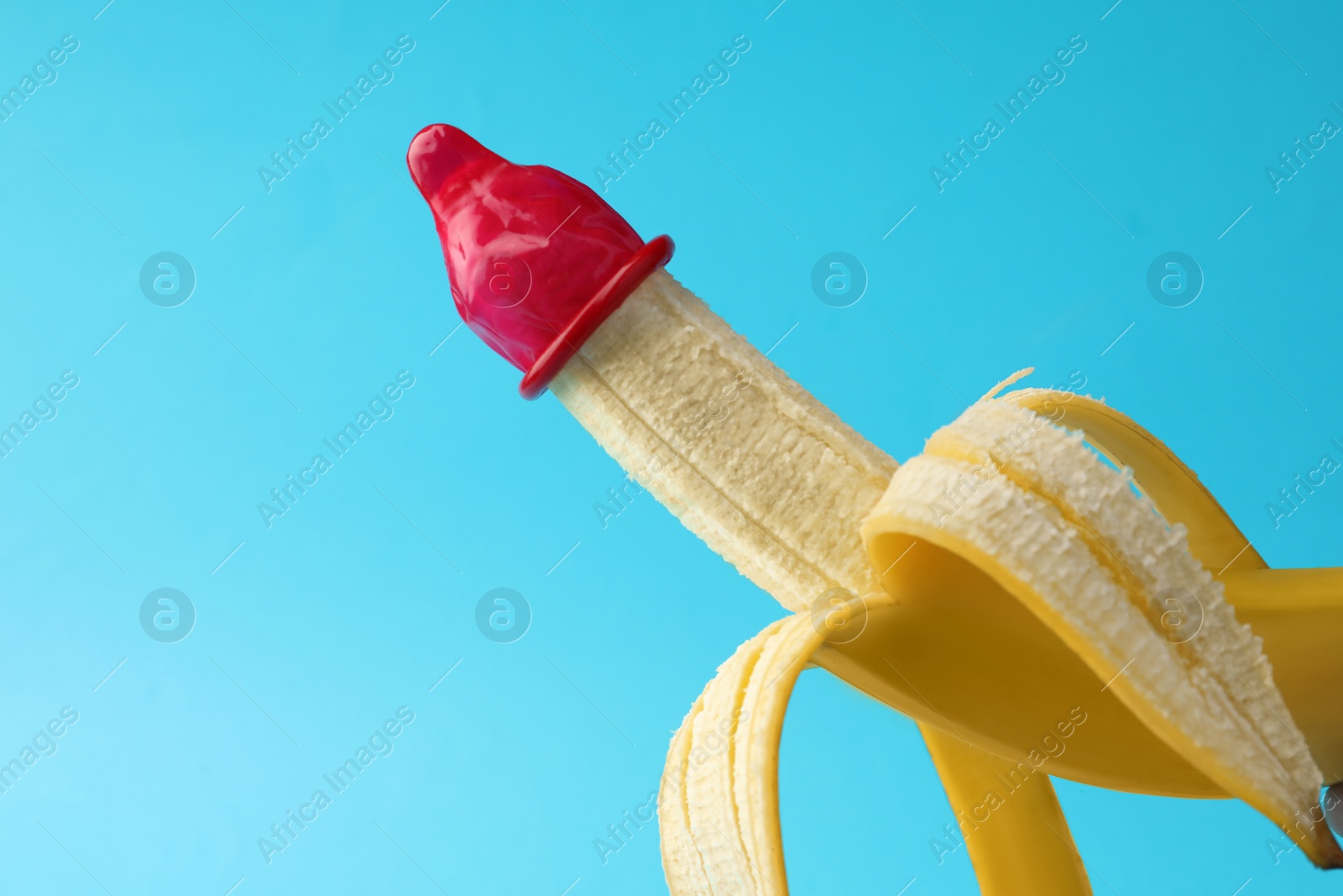 Photo of Banana with condom on light blue background, space for text. Safe sex concept