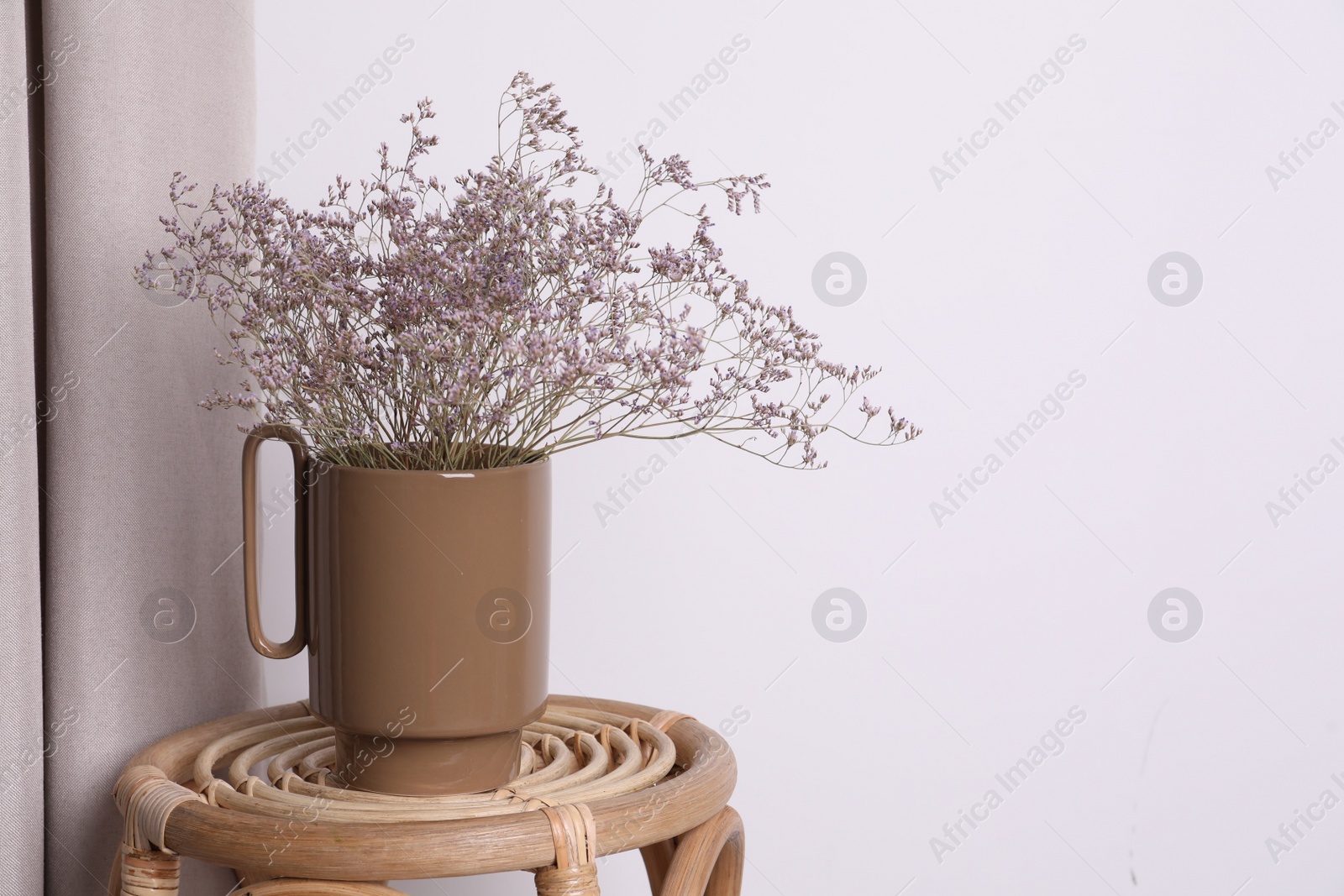 Photo of Ceramic vase with dry flowers on wicker table near white wall. Space for text