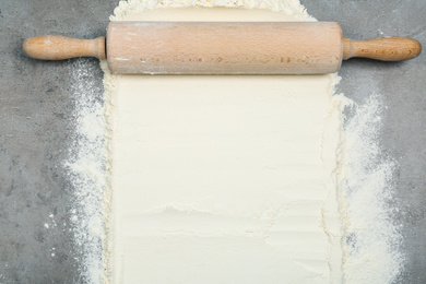 Flour and rolling pin on light grey table, top view. Space for text