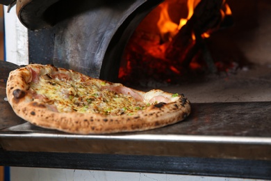 Taking out tasty pizza from oven in restaurant kitchen