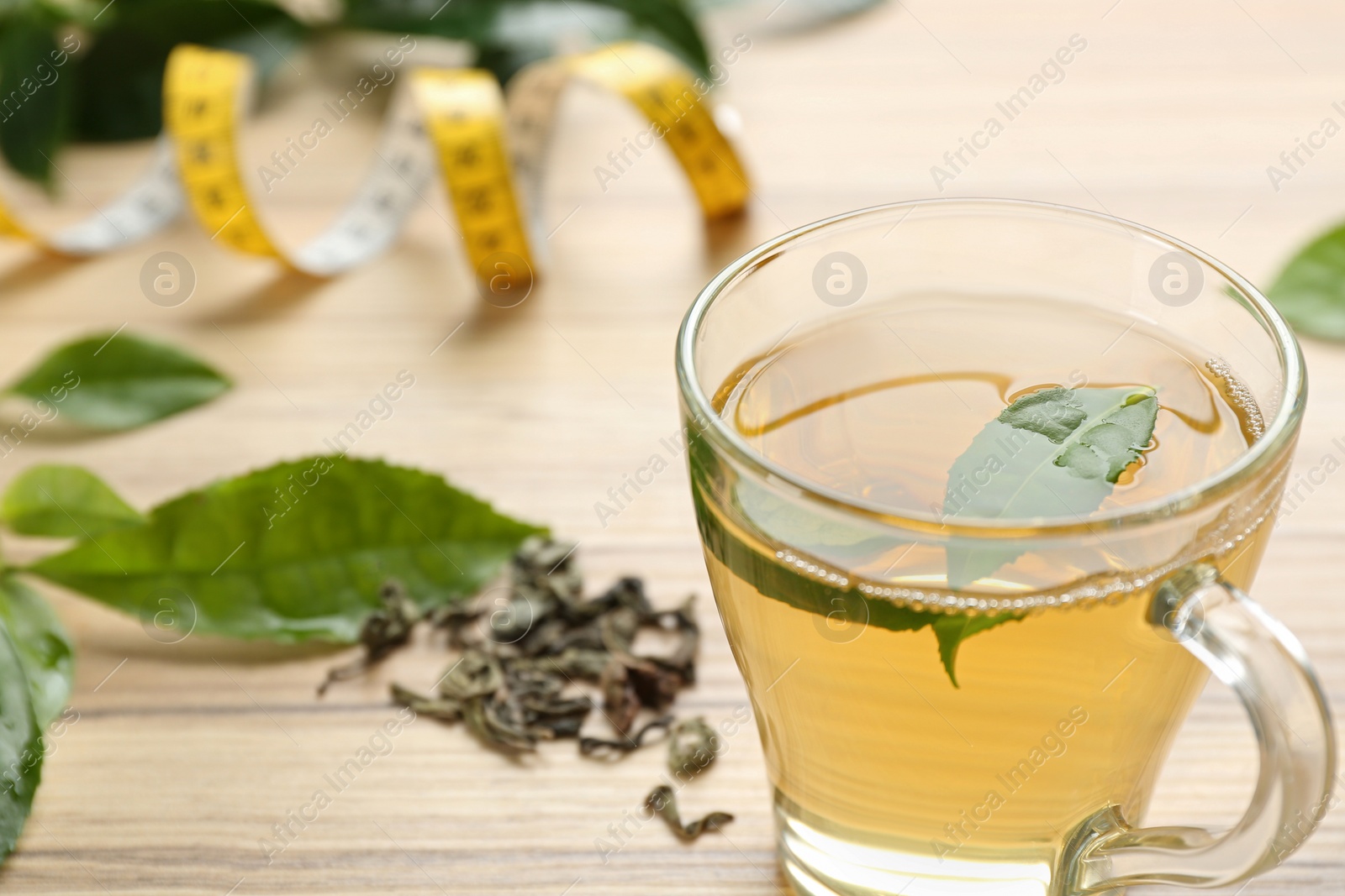 Photo of Herbal diet tea and measuring tape on wooden table, closeup. Space for text