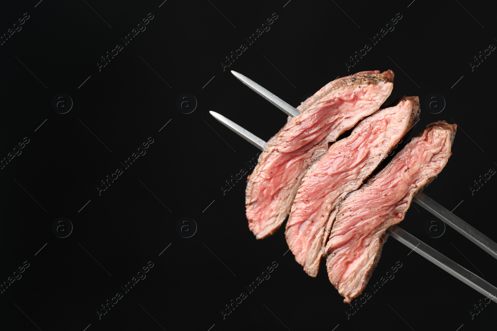 Photo of Meat fork with grilled beef pieces on black background, closeup. Space for text