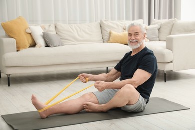 Photo of Senior man doing exercise with fitness elastic band on mat at home