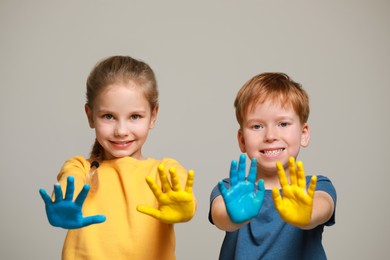 Photo of Little girl and boy with hands painted in Ukrainian flag colors on light grey background. Love Ukraine concept