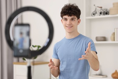 Photo of Smiling teenage blogger explaining something while streaming at home