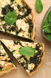 Delicious homemade quiche and fresh spinach leaves on parchment paper, flat lay