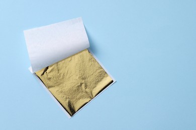 Photo of Edible gold leaf sheet on light blue background, top view. Space for text