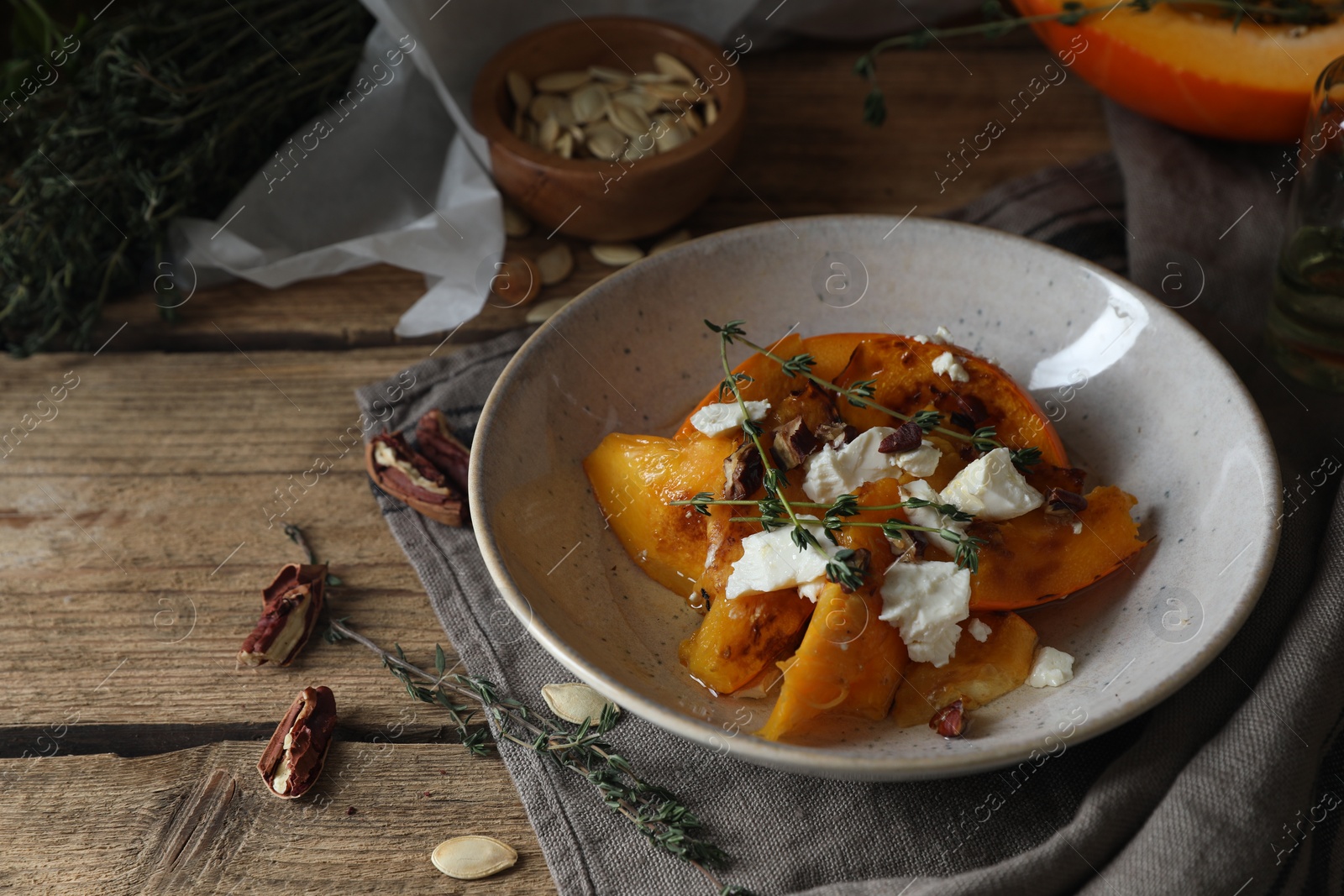 Photo of Baked pumpkin slices served with cheese, thyme and pecans on wooden table, space for text