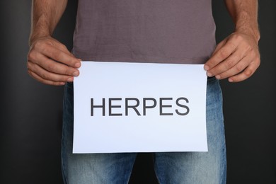 Man holding paper with word Herpes on black background, closeup