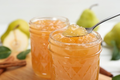 Delicious pear jam and spoon on blurred background, closeup