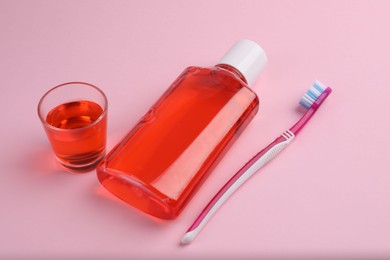Photo of Fresh mouthwash in bottle, glass and toothbrush on pink background, closeup