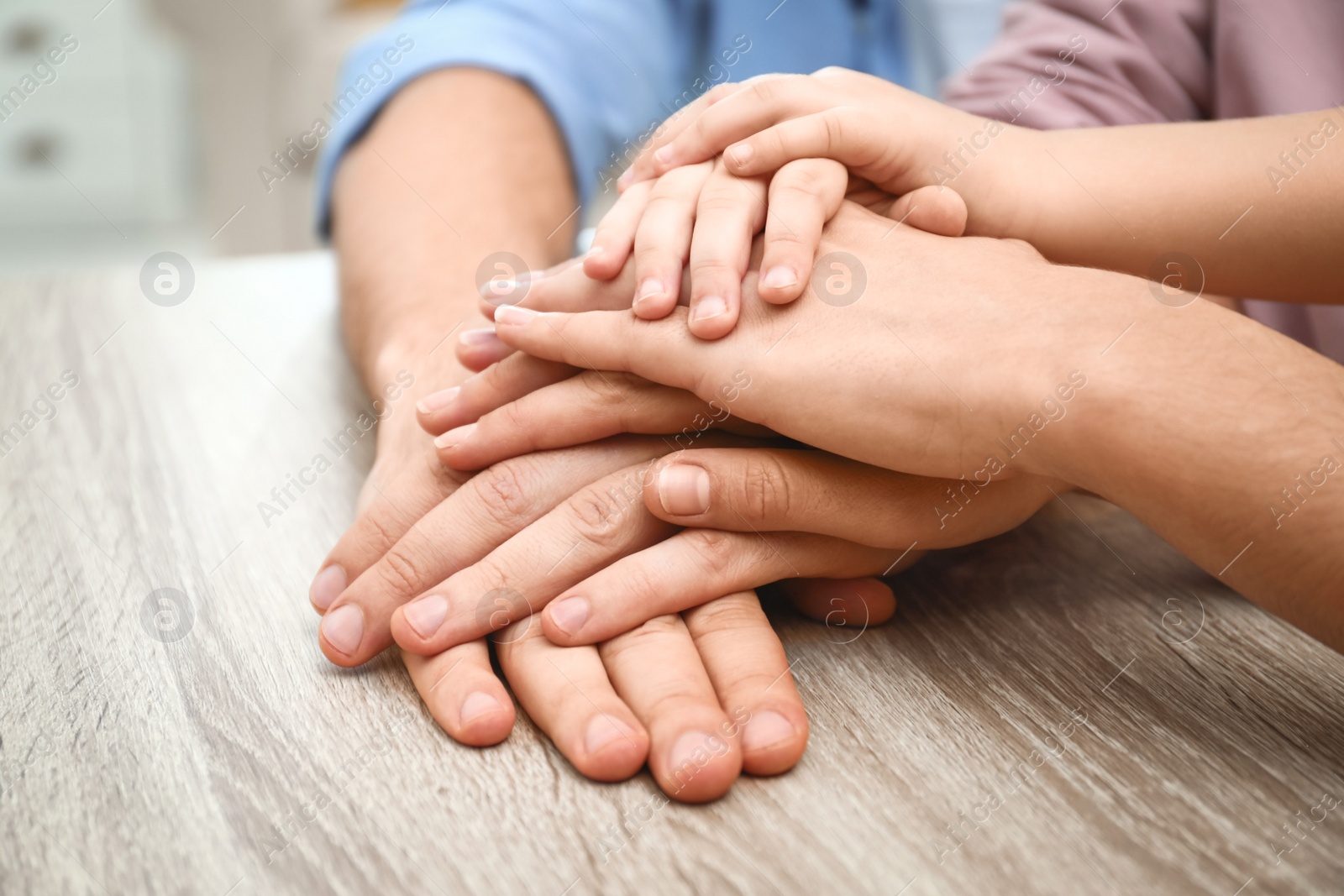 Photo of Happy family holding hands at wooden table indoors, closeup view