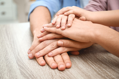 Photo of Happy family holding hands at wooden table indoors, closeup view