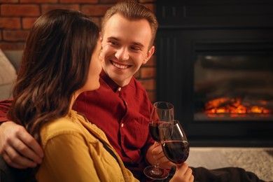 Photo of Happy lovely couple with glasses of wine resting together near fireplace at home