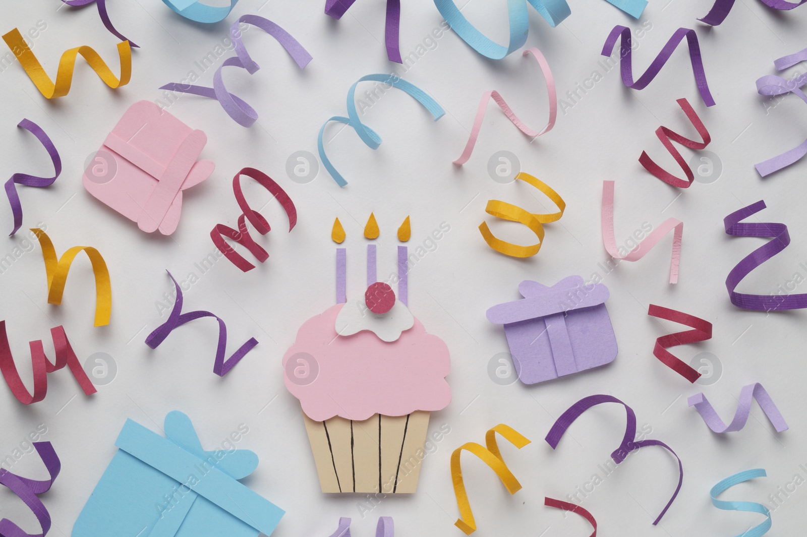 Photo of Birthday party. Paper cupcake, gift boxes and confetti on white background, flat lay
