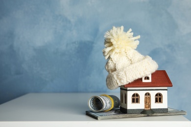 Photo of House model with warm hat, money and space for text against color background. Heating expenses