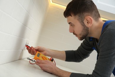 Photo of Professional electrician with tester checking voltage indoors