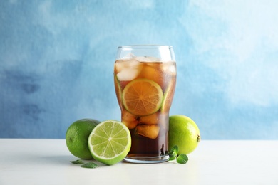 Photo of Glass of coke with ice cubes and limes on table against color background