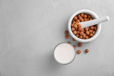 Photo of Glass with hazelnut milk and nuts in mortar on light background, top view