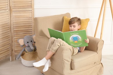 Photo of Little boy reading book in armchair at home