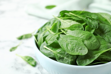 Photo of Bowl of fresh green healthy spinach on white marble table, closeup