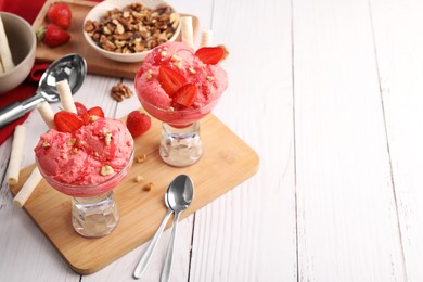 Photo of Delicious scoops of strawberry ice cream with wafer sticks and nuts in glass dessert bowls served on white wooden table. Space for text