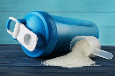 Photo of Measuring scoop of protein powder and shaker on blue wooden table, closeup