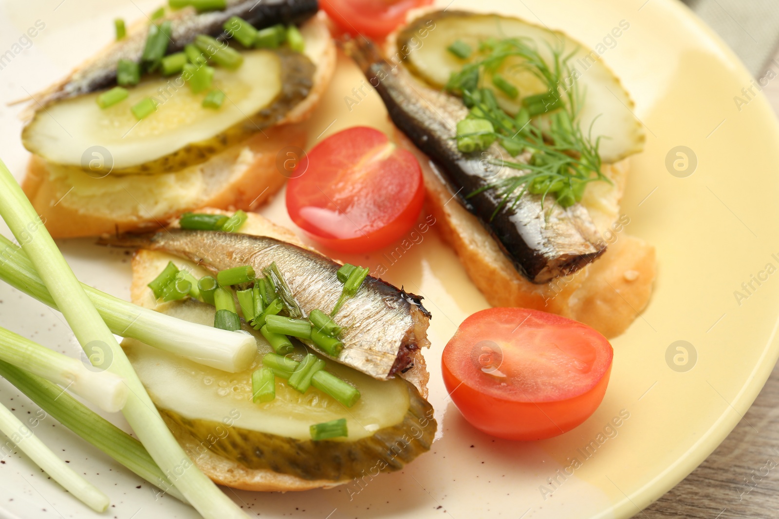 Delicious sandwiches with sprats, pickled cucumber and green onion served with tomato on wooden table, closeup Photo of Delicious sandwiches with sprats, pickled cucumber and green onion served with tomato on wooden table, closeup