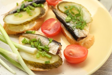 Photo of Delicious sandwiches with sprats, pickled cucumber and green onion served with tomato on wooden table, closeup