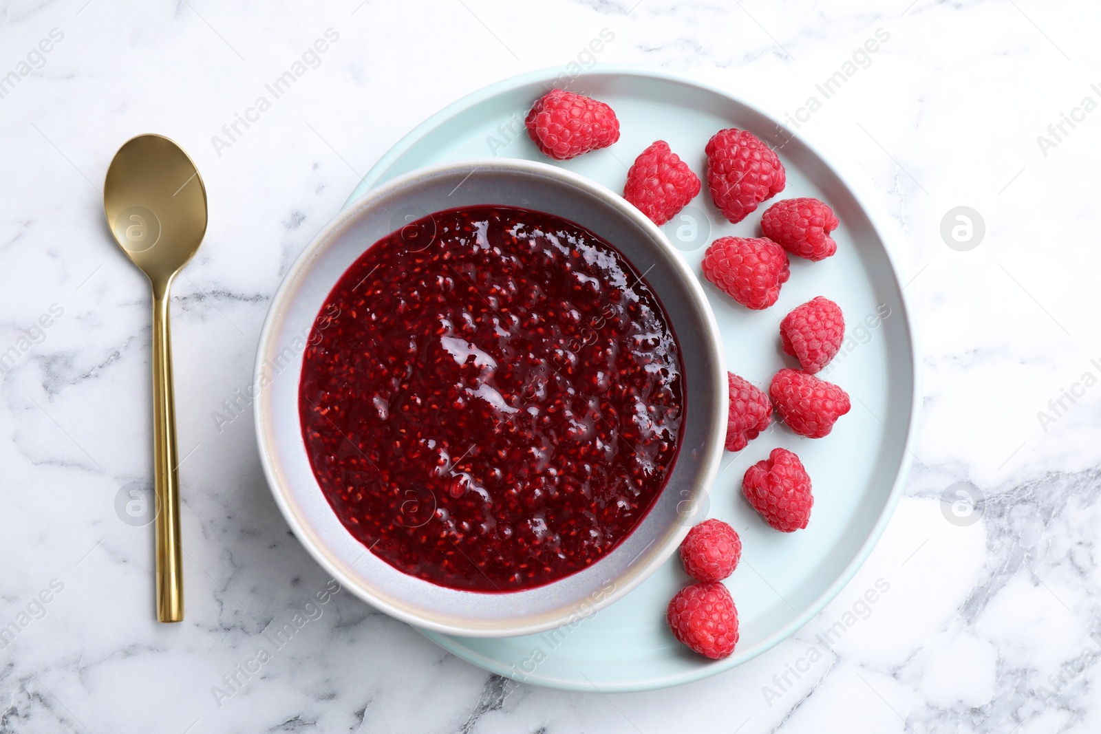 Photo of Delicious jam and fresh raspberries on white marble table, flat lay