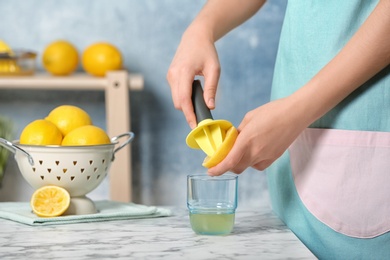 Photo of Woman squeezing lemon juice with reamer into glass on table