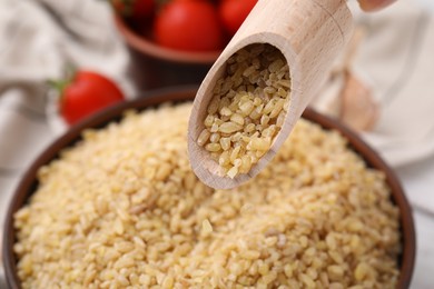 Photo of Pouring raw bulgur from scoop into bowl, closeup