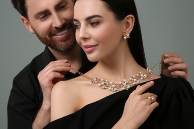 Photo of Man putting elegant necklace on beautiful woman against grey background, closeup