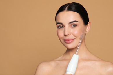 Photo of Woman using high frequency darsonval device on beige background. Space for text