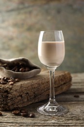 Photo of Coffee cream liqueur in glass and beans on wooden table