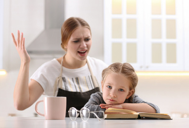 Mother scolding her daughter while helping with homework in kitchen