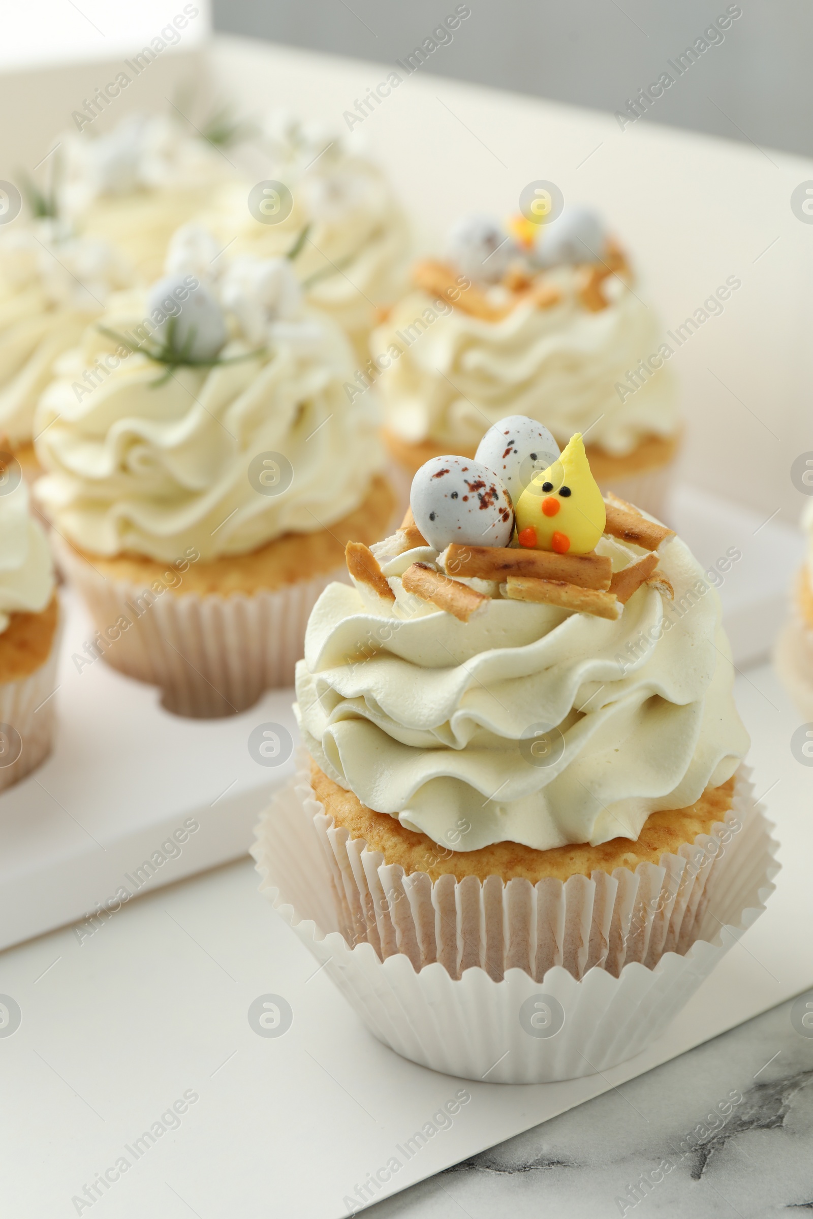 Photo of Tasty Easter cupcakes with vanilla cream on white marble table, closeup