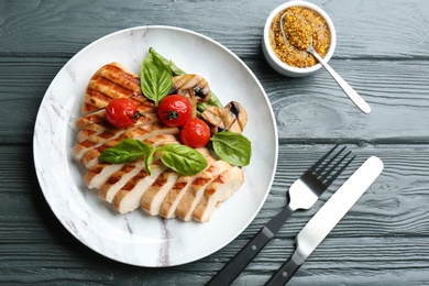 Photo of Tasty grilled chicken fillet with vegetables served on grey wooden table, flat lay