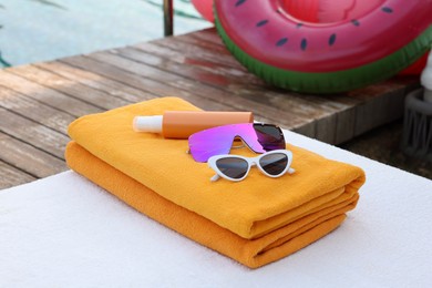 Photo of Beach towels, sunglasses and sunscreen on sunbed near outdoor swimming pool. Luxury resort