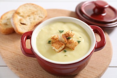 Photo of Tasty potato soup with croutons and rosemary in ceramic pot on white table, closeup