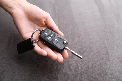 Photo of Woman holding car flip key on grey background, closeup. Space for text