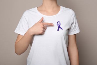 Photo of Woman wearing purple ribbon on grey background, closeup. Domestic violence awareness