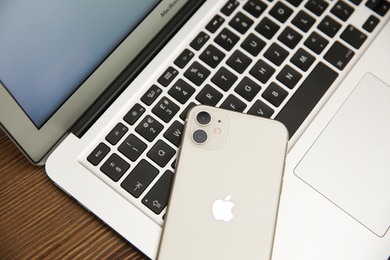 Photo of MYKOLAIV, UKRAINE - JULY 20, 2020: iPhone 11 and MacBook on wooden table, closeup