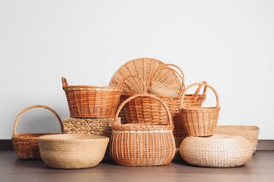 Photo of Many different wicker baskets made of natural material on floor near light wall